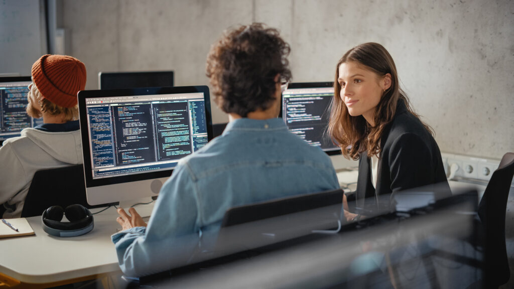 smart young students studying in university with diverse multiethnic classmates. scholars collaborate in college room on computer science project, writing software code in successful teamwork.