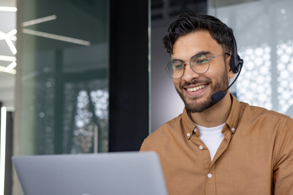 smiling customer service representative with headset working on laptop in office